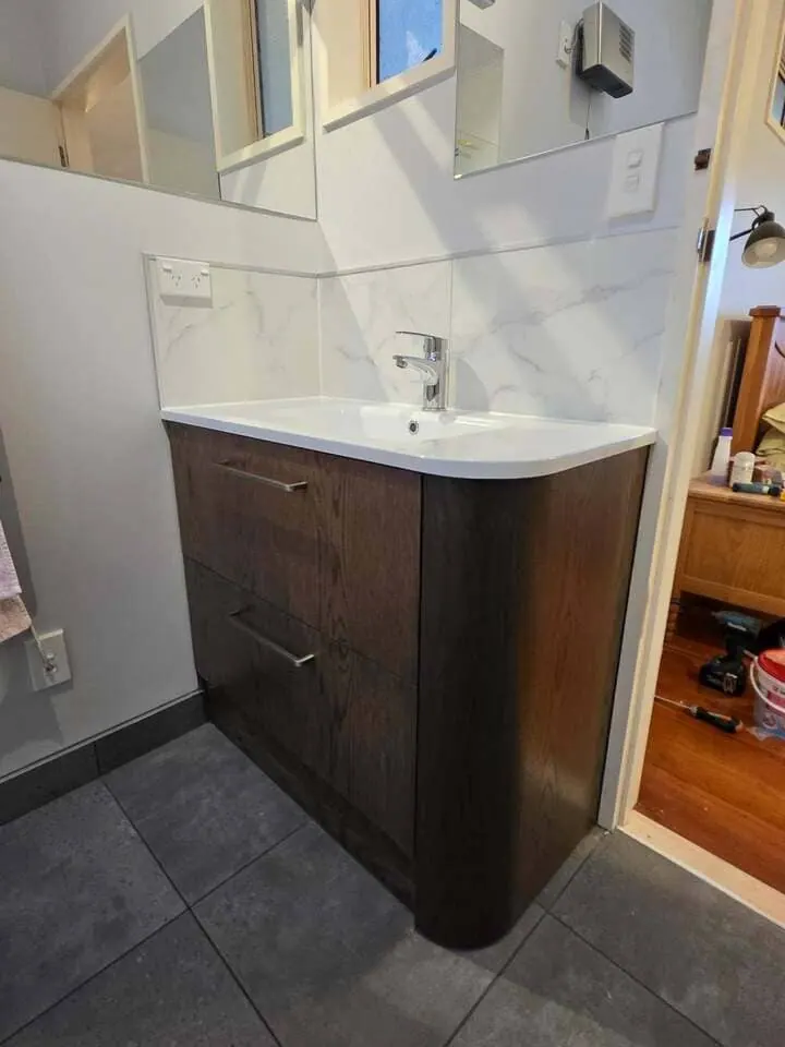 Curved-end timber-look bathroom vanity with a marble-look tiled splashback