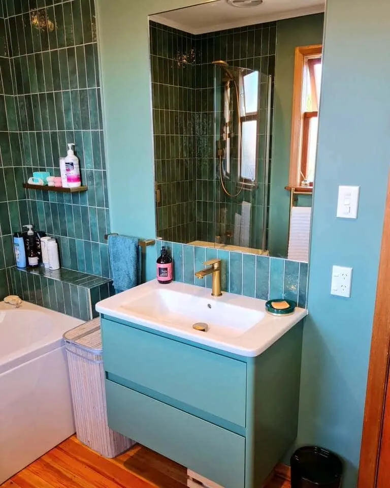 Wall-hung green vanity with brass tap and green tiles carried up behind a frameless mirror